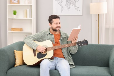 Photo of Relaxing hobby. Smiling man with guitar and book on sofa at home