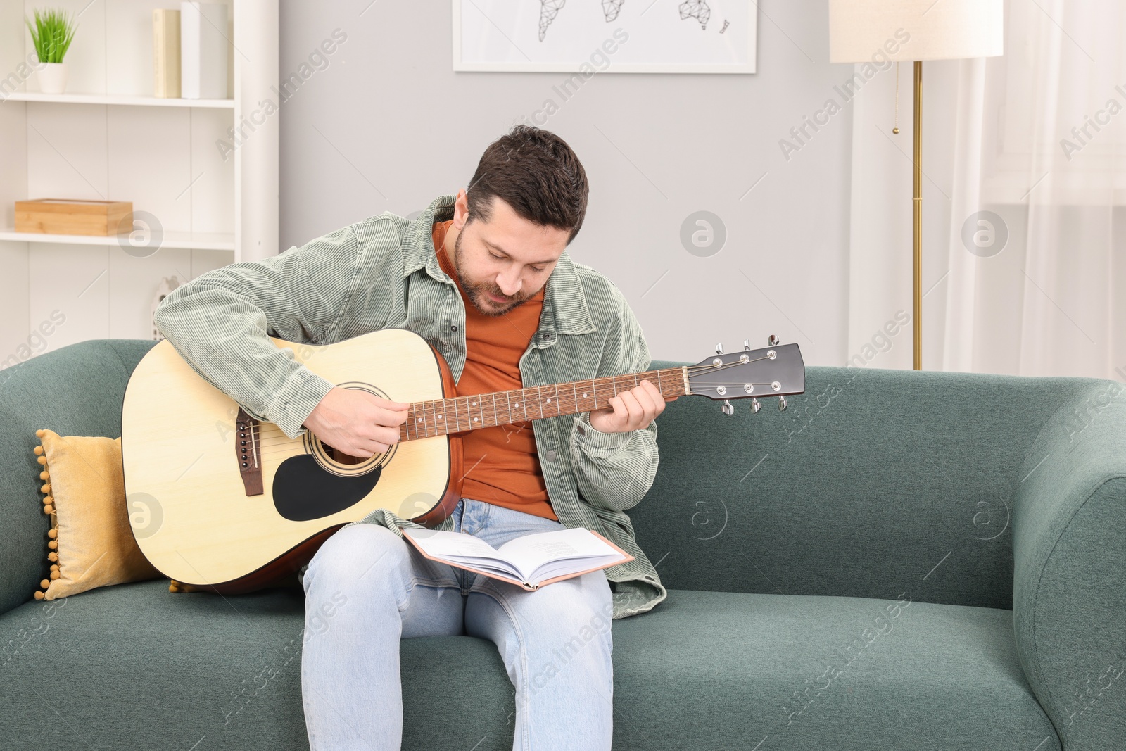 Photo of Relaxing hobby. Man with guitar and book on sofa at home