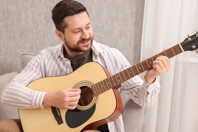 Photo of Relaxing hobby. Smiling man playing guitar at home