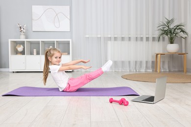 Photo of Little girl exercising with online coach via laptop at home. Sport activity