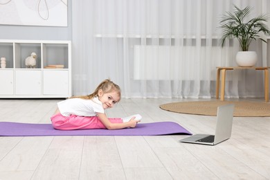 Photo of Little girl exercising with online coach via laptop at home. Sport activity