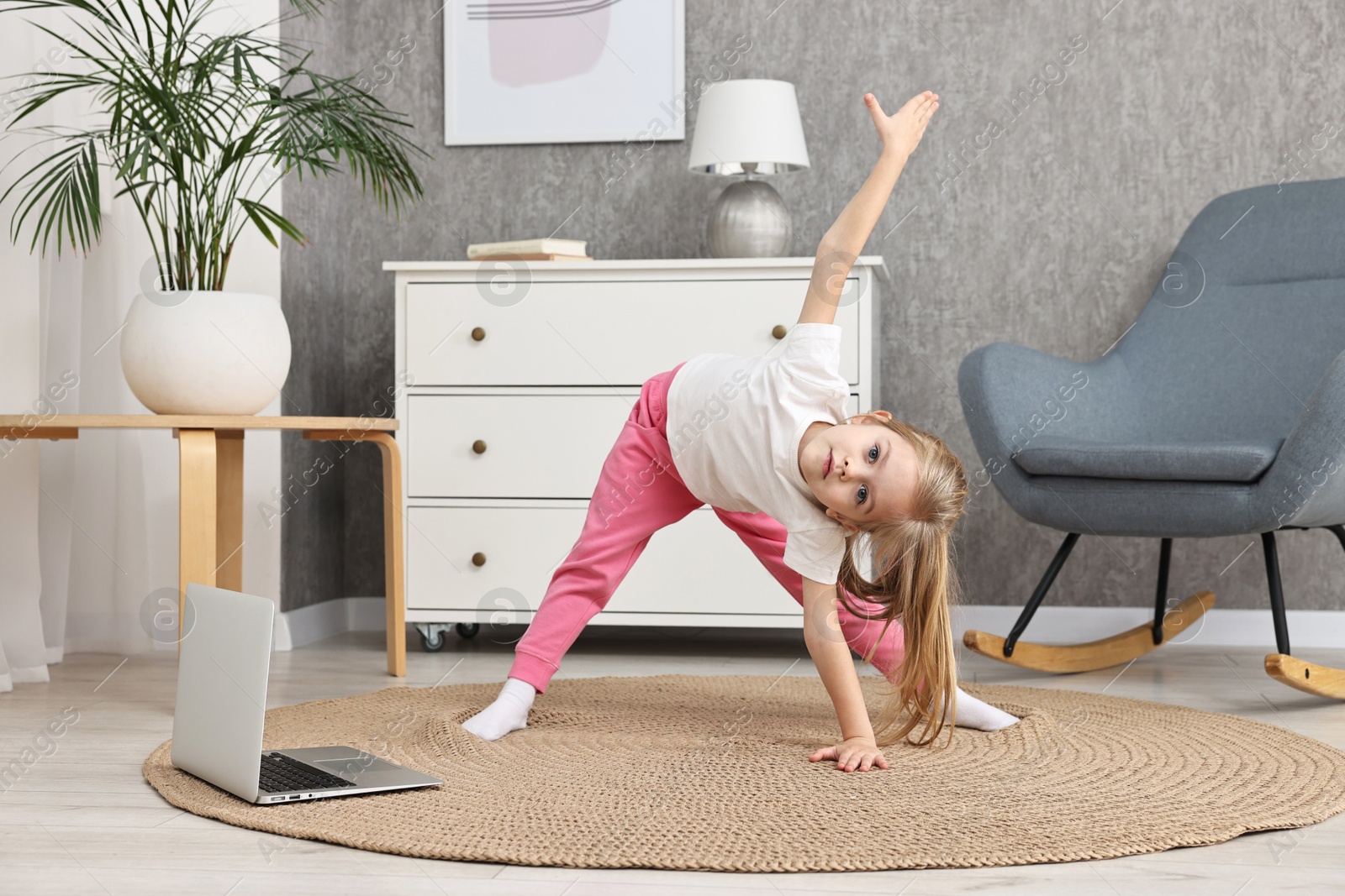 Photo of Little girl exercising with online coach via laptop at home. Sport activity