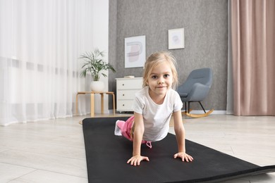 Photo of Little girl exercising on fitness mat at home. Sport activity