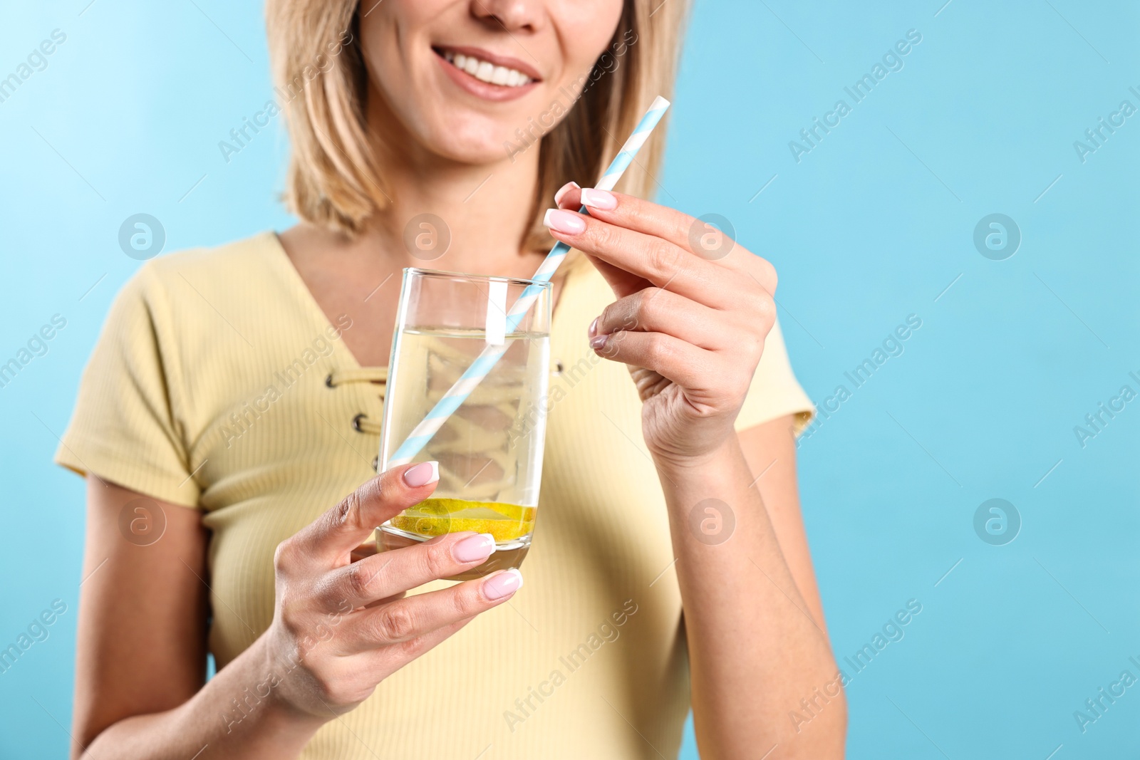 Photo of Woman with glass of lemonade on light blue background, closeup. Refreshing drink