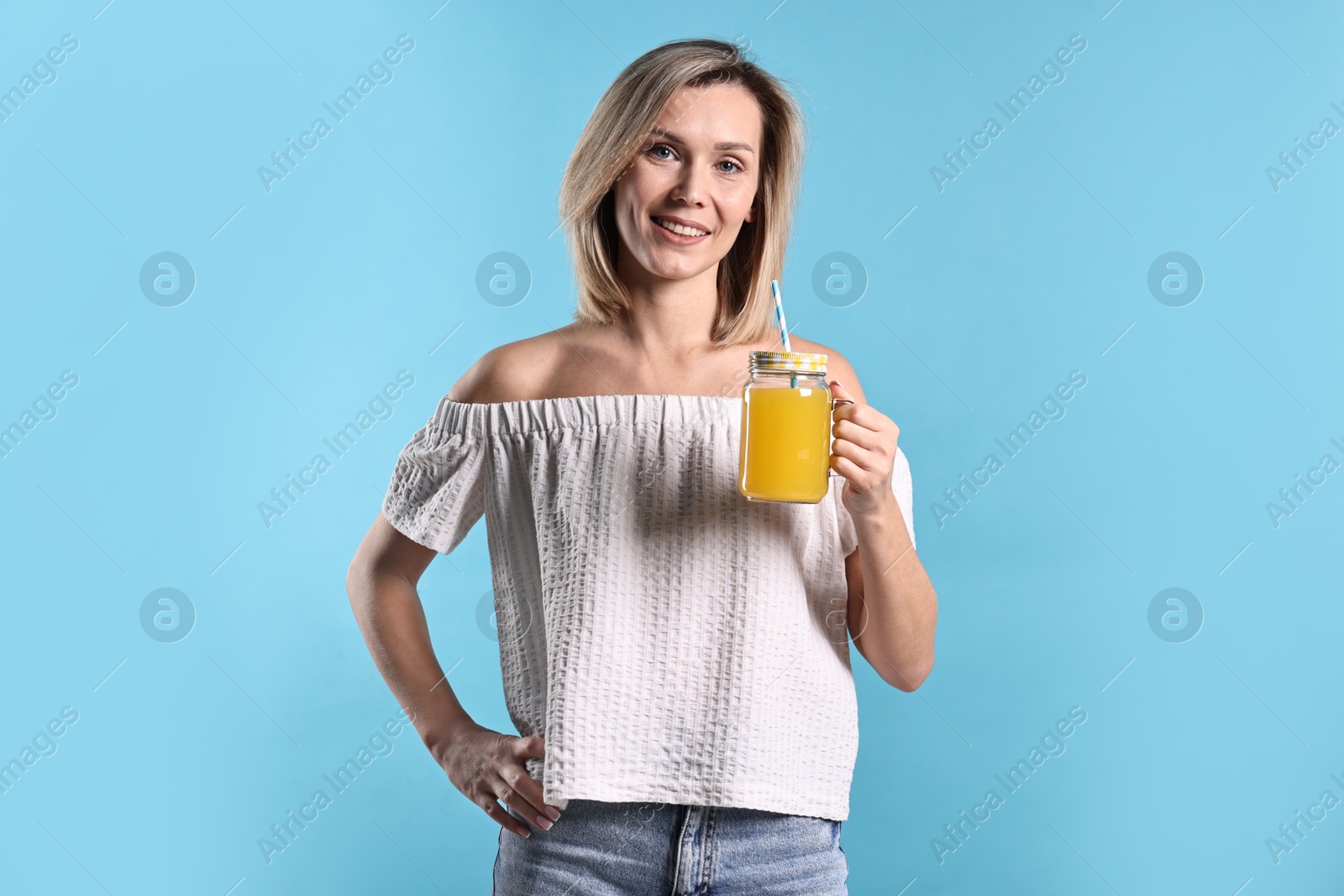 Photo of Woman with mason jar of orange juice on light blue background. Refreshing drink