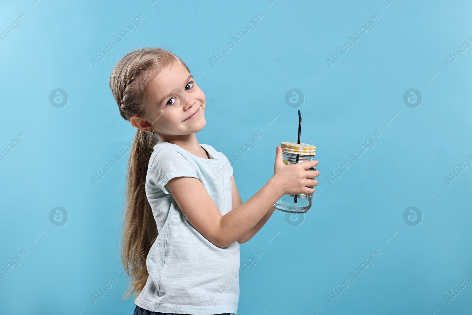 Photo of Girl with mason jar of cucumber water on light blue background. Refreshing drink