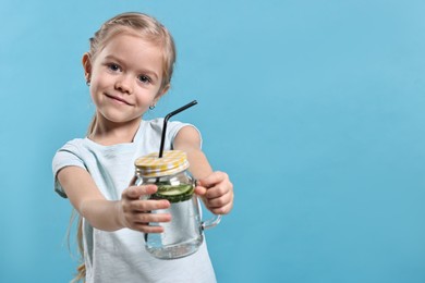 Photo of Girl with mason jar of cucumber water on light blue background, space for text. Refreshing drink