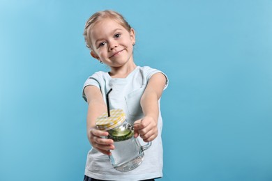 Photo of Girl with mason jar of cucumber water on light blue background. Refreshing drink