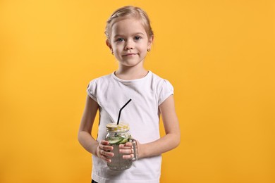 Photo of Girl with mason jar of cucumber water on orange background. Refreshing drink