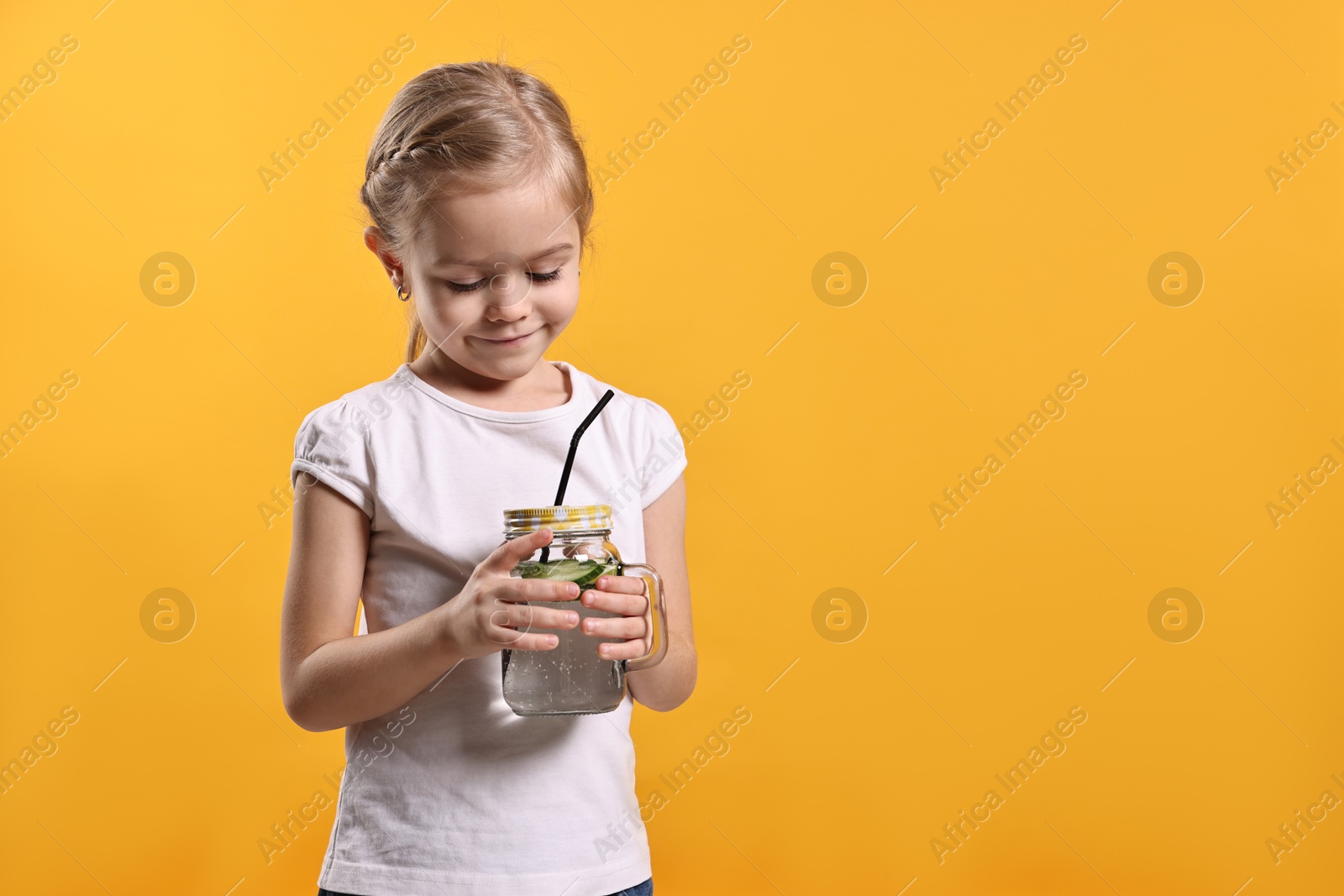 Photo of Girl with mason jar of cucumber water on orange background, space for text. Refreshing drink