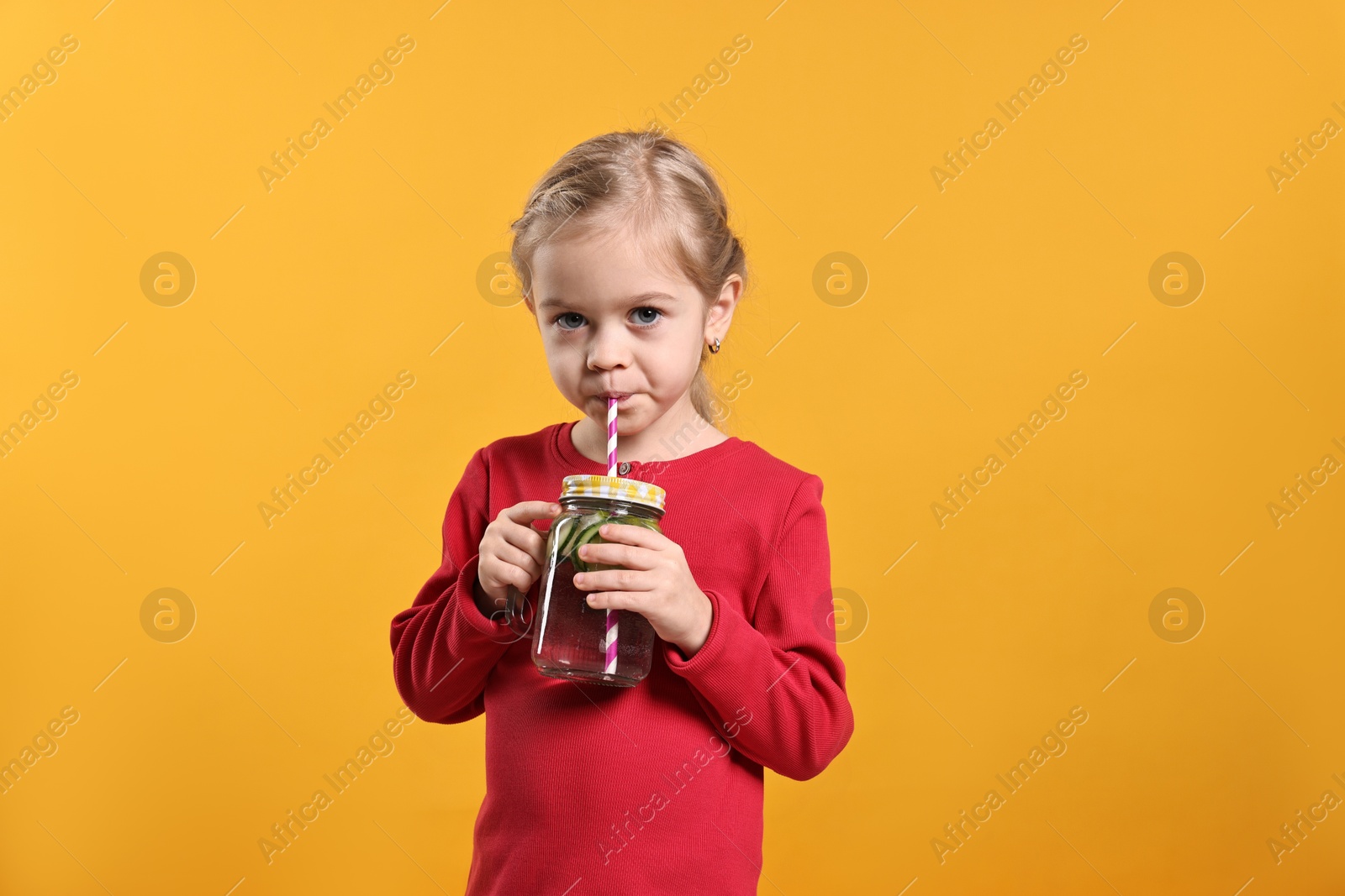 Photo of Girl drinking tasty cucumber water on orange background. Refreshing drink