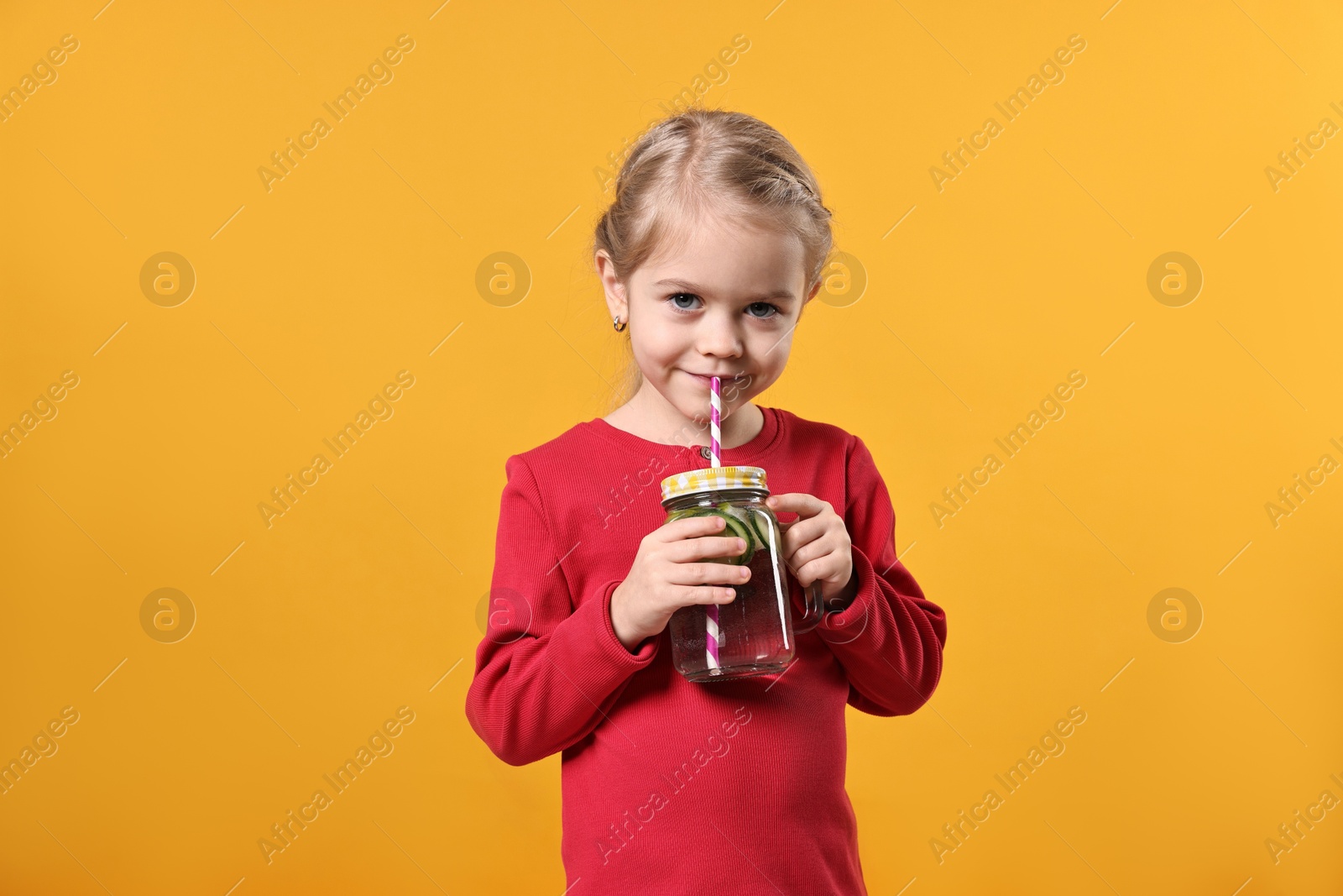 Photo of Girl drinking tasty cucumber water on orange background. Refreshing drink