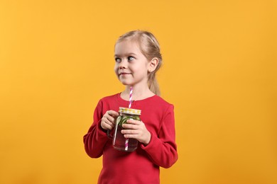 Photo of Girl with mason jar of cucumber water on orange background. Refreshing drink