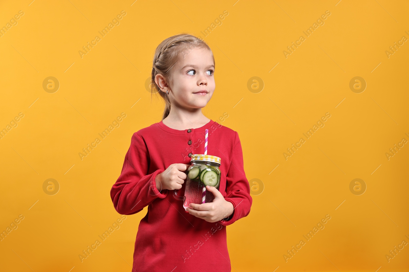 Photo of Girl with mason jar of cucumber water on orange background. Refreshing drink