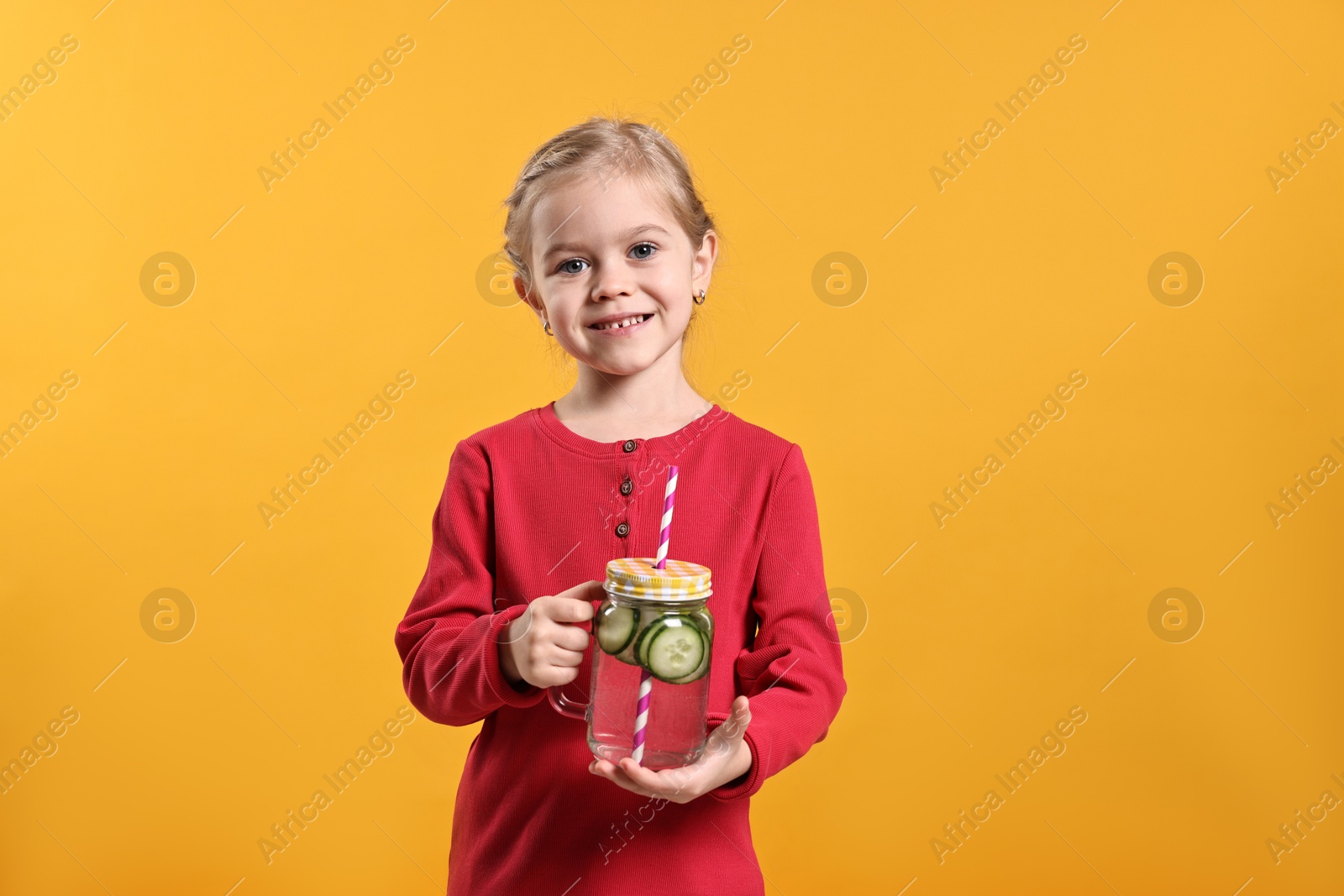 Photo of Girl with mason jar of cucumber water on orange background. Refreshing drink