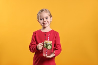 Photo of Girl with mason jar of cucumber water on orange background. Refreshing drink