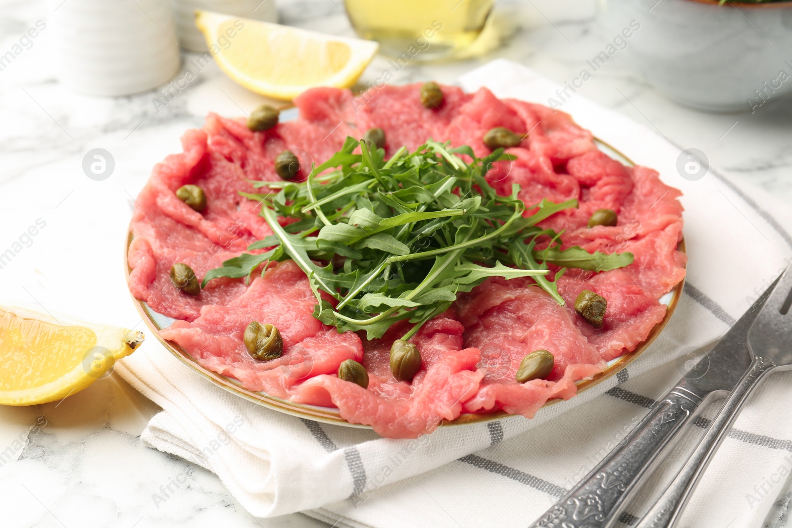 Photo of Delicious beef carpaccio served on light marble table, closeup