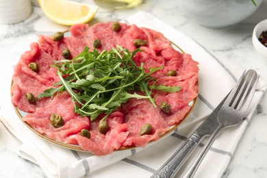 Photo of Delicious beef carpaccio served on light marble table, closeup