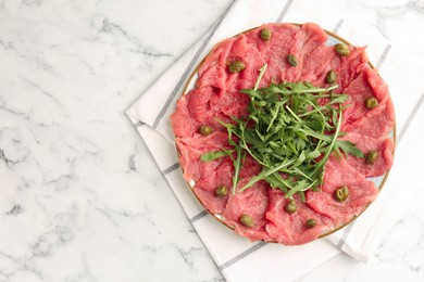 Photo of Delicious beef carpaccio with arugula and capers on white marble table, top view. Space for text