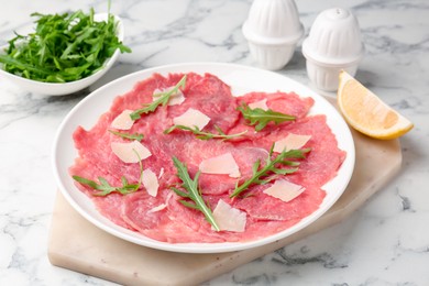 Photo of Delicious beef carpaccio with arugula, cheese and lemon on white marble table, closeup