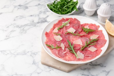 Delicious beef carpaccio with arugula and cheese on white marble table, closeup. Space for text