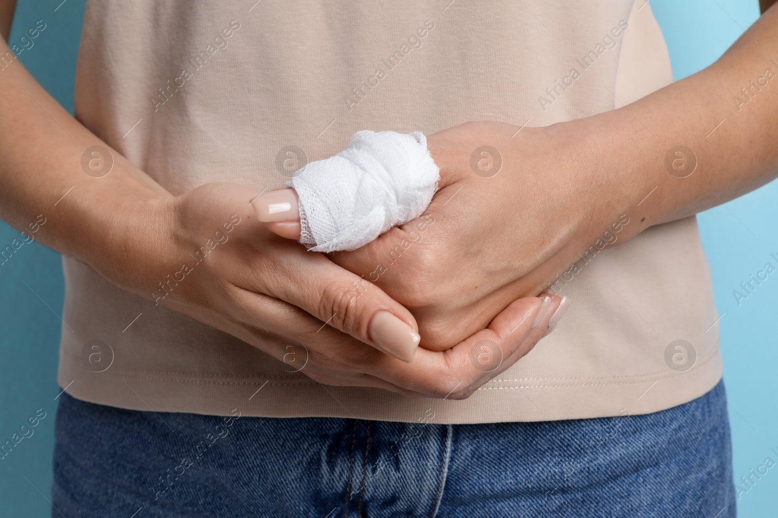 Photo of Woman with medical bandage on finger against light blue background, closeup