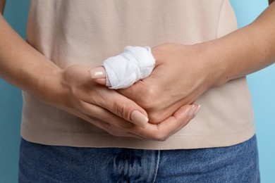 Photo of Woman with medical bandage on finger against light blue background, closeup