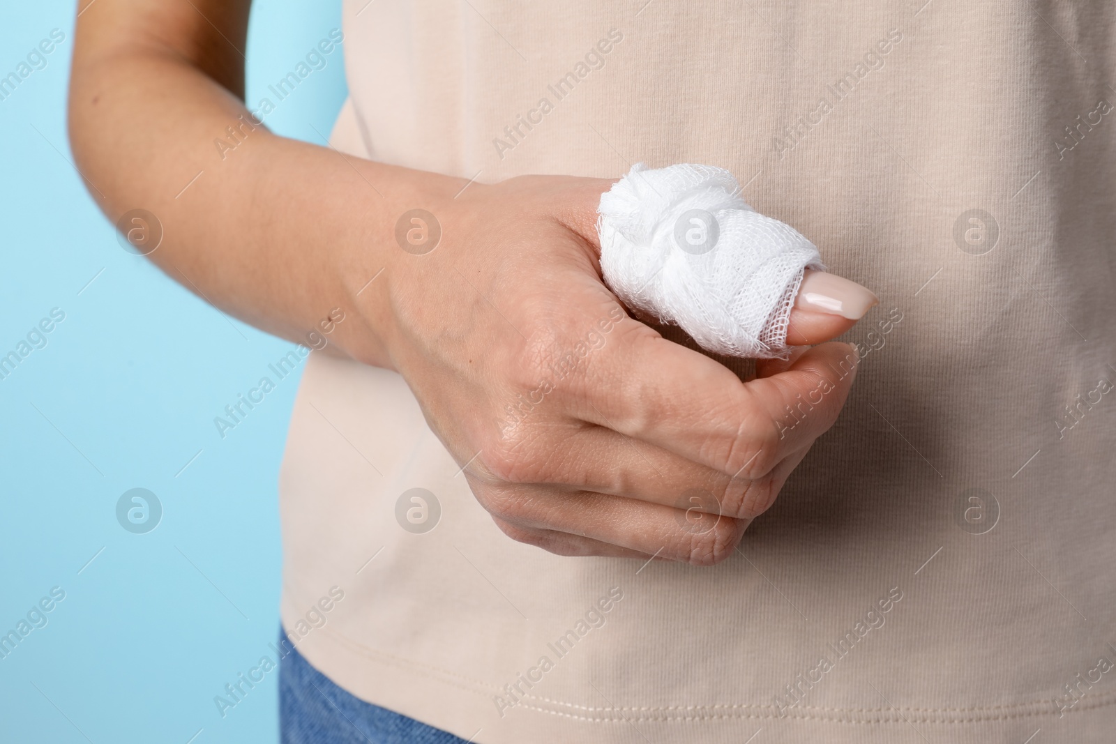 Photo of Woman with medical bandage on finger against light blue background, closeup