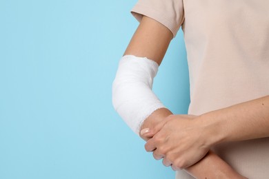 Photo of Woman with medical bandage on elbow against light blue background, closeup. Space for text