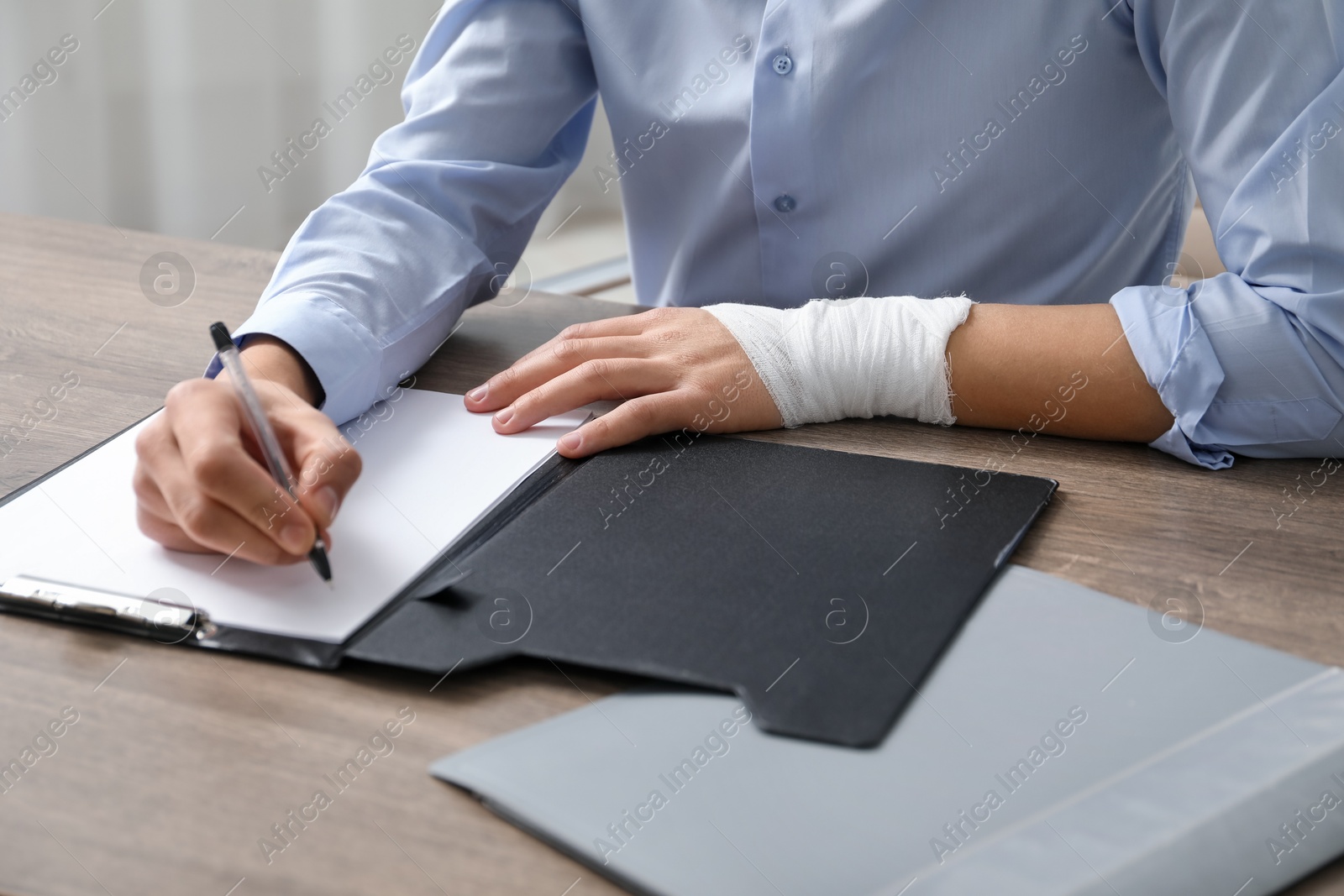 Photo of Man with medical bandage on his wrist working at wooden table indoors, closeup