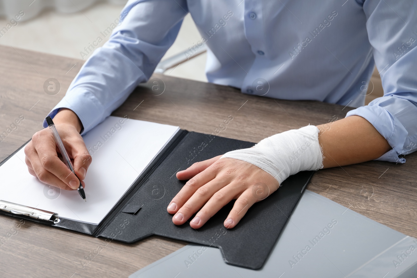 Photo of Man with medical bandage on his wrist working at wooden table indoors, closeup