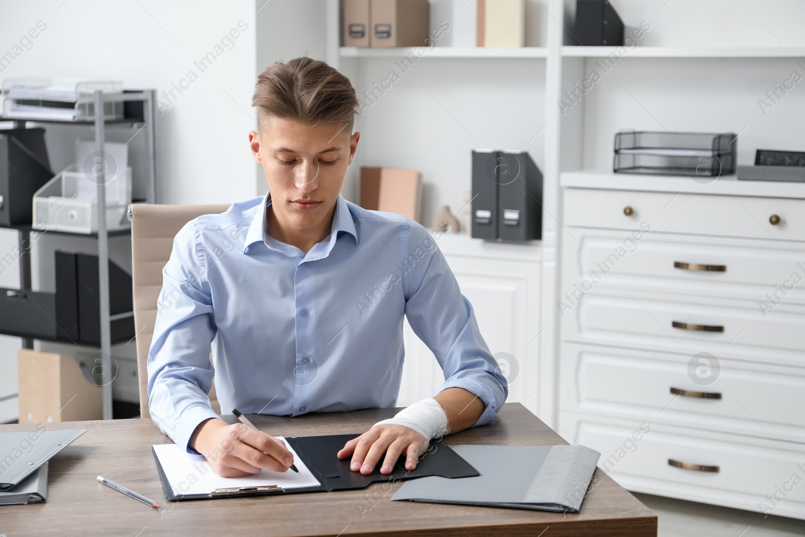 Photo of Man with medical bandage on his wrist working at wooden table indoors