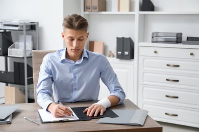 Man with medical bandage on his wrist working at wooden table indoors