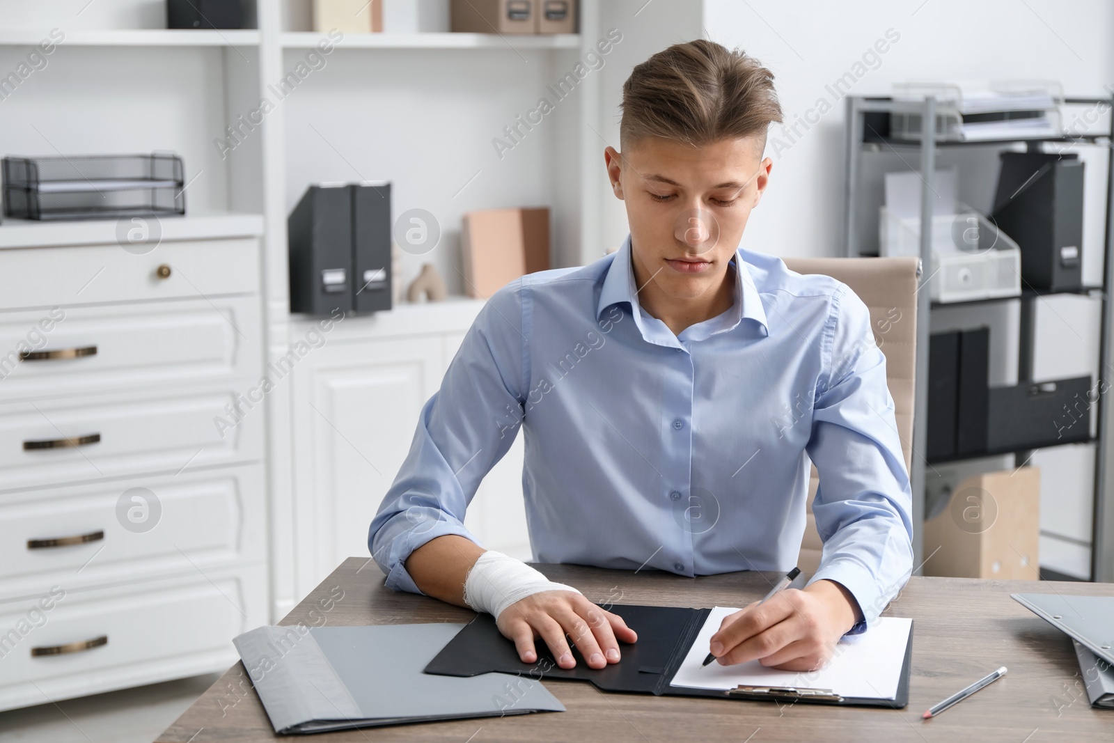 Photo of Man with medical bandage on his wrist working at wooden table indoors