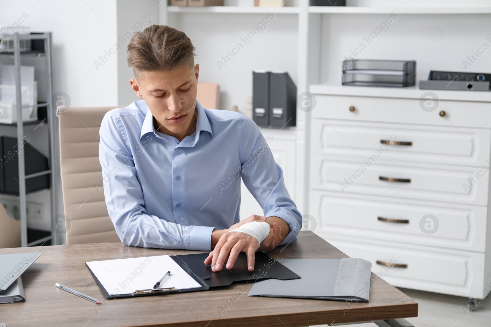 Photo of Man with medical bandage on his wrist at wooden table indoors