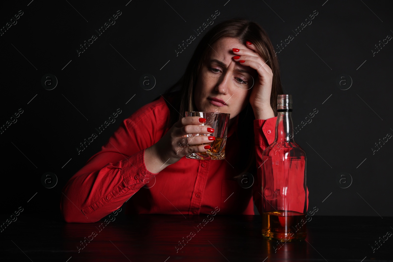 Photo of Alcohol addiction. Miserable woman drinking whiskey at table in dark