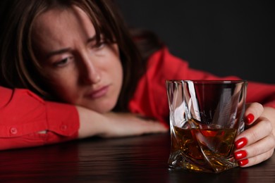 Photo of Alcohol addiction. Miserable woman with whiskey at table in dark, selective focus