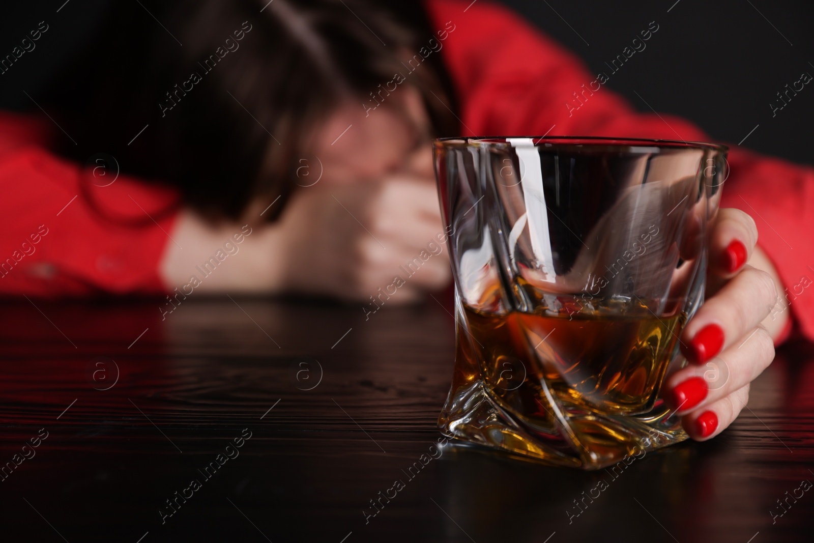 Photo of Alcohol addiction. Miserable woman with whiskey at table in dark, selective focus