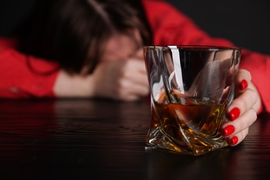 Photo of Alcohol addiction. Miserable woman with whiskey at table in dark, selective focus