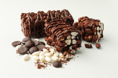 Photo of Delicious chocolate puffed rice bars and cacao chips on white table, closeup