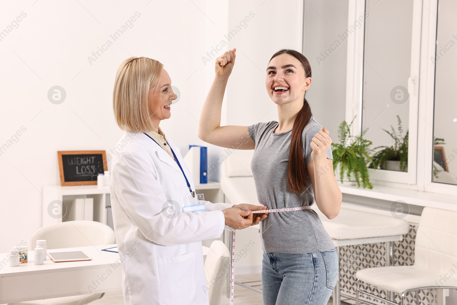 Photo of Happy woman lost weight. Nutritionist measuring patient's waist with tape in clinic