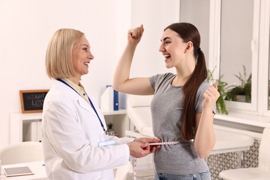 Photo of Happy woman lost weight. Nutritionist measuring patient's waist with tape in clinic