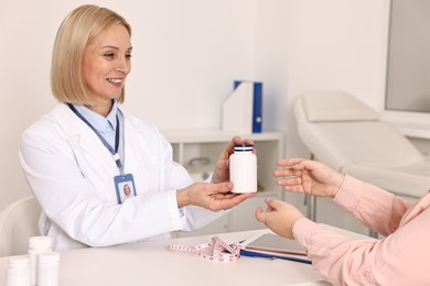 Photo of Weight loss. Smiling nutritionist giving medical bottle with pills to patient at table in clinic