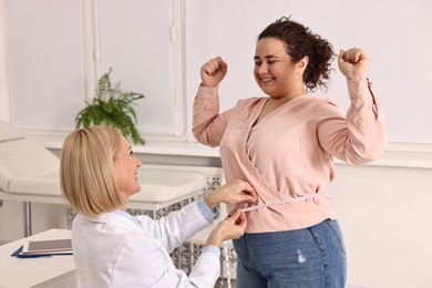 Photo of Happy woman lost weight. Smiling nutritionist measuring patient's waist with tape in clinic