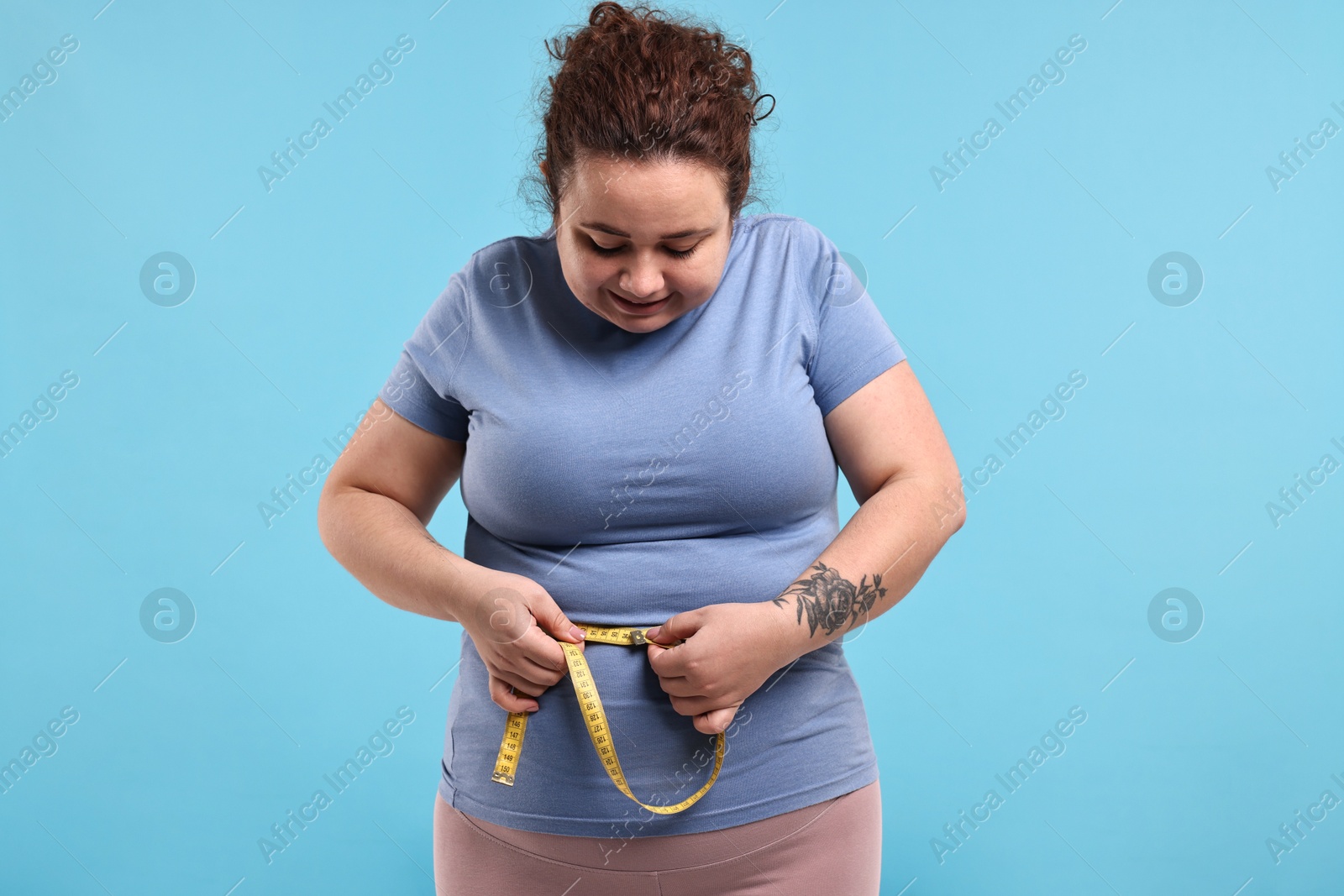 Photo of Weight loss. Plus size woman measuring waist with tape on light blue background