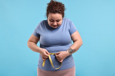 Photo of Weight loss. Plus size woman measuring waist with tape on light blue background