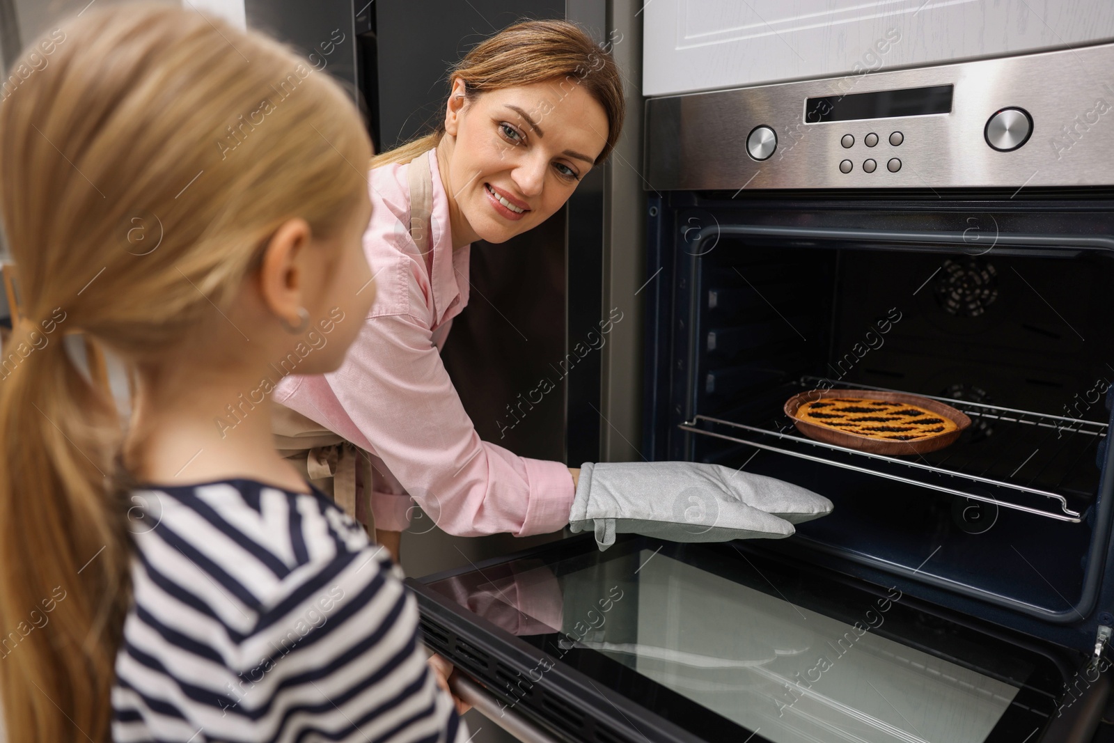 Photo of Mother and her daughter taking out pie from oven in kitchen