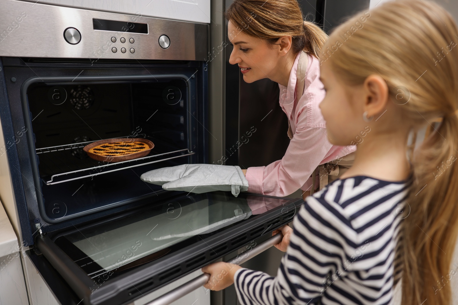 Photo of Mother and her daughter taking out pie from oven in kitchen