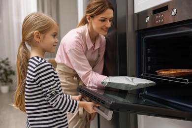 Photo of Mother and her daughter taking out pie from oven in kitchen, selective focus