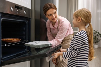 Photo of Mother and her daughter taking out pie from oven in kitchen